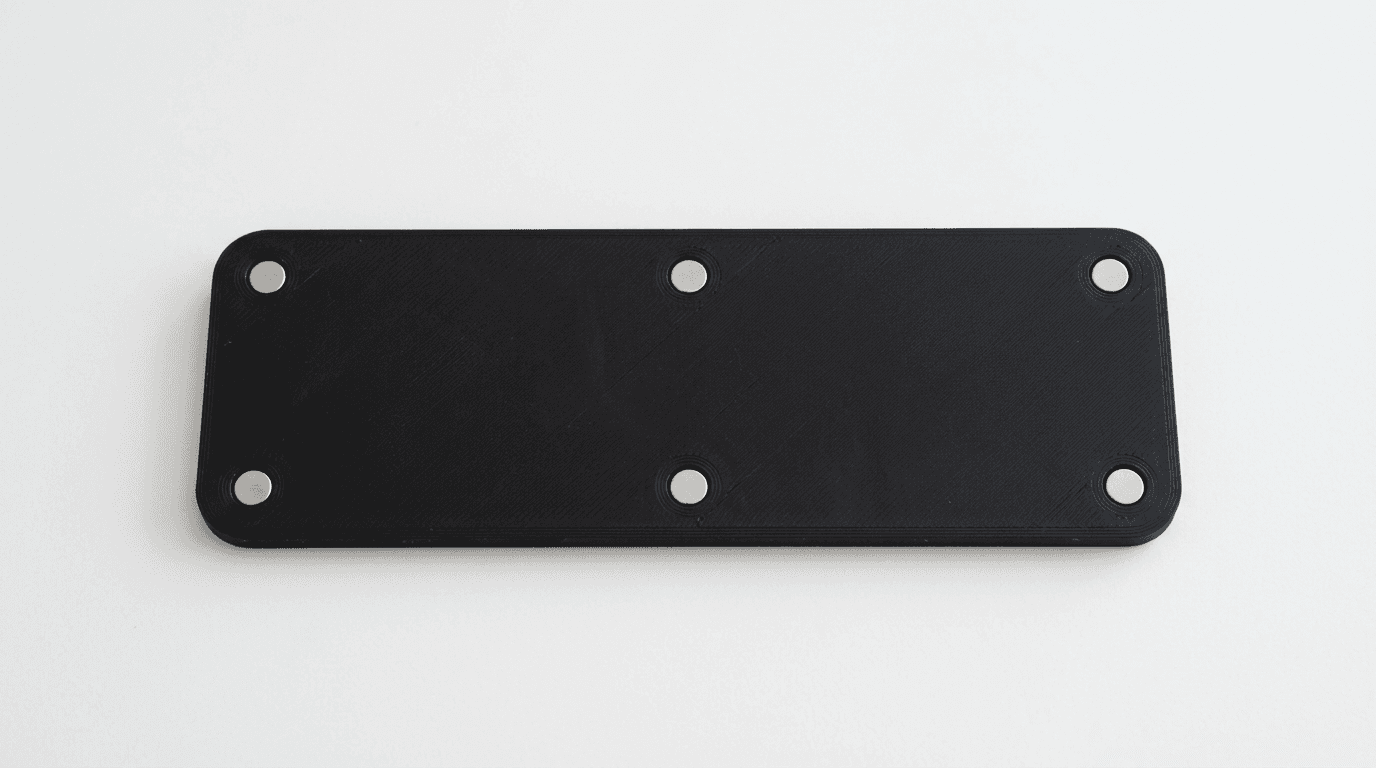 Back of a black 3D-printed number plate with small neodymium magnets embedded flush in each corner and along the edges for magnetic mounting